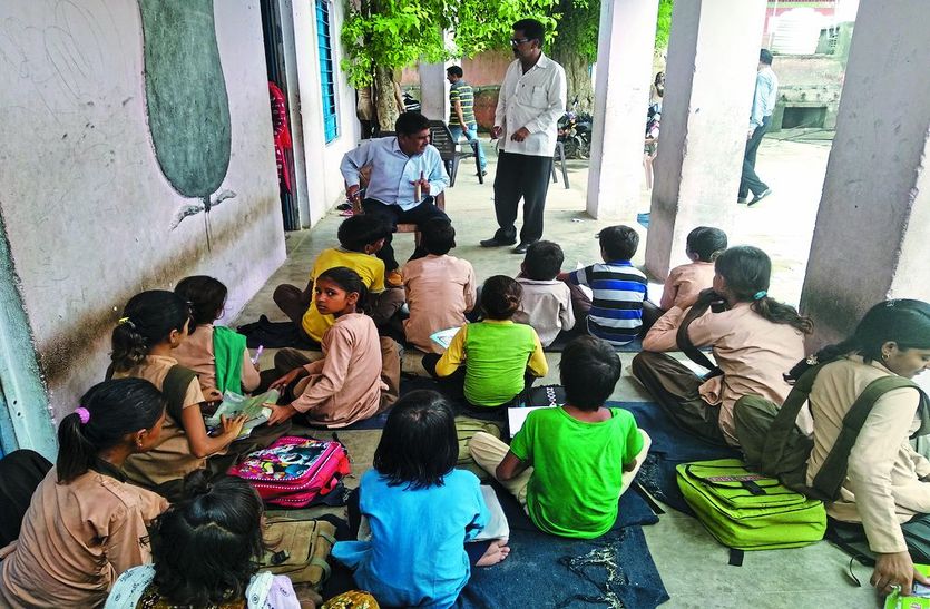 भवन की कमी से बरामदे में पढ़ते विद्यार्थी।