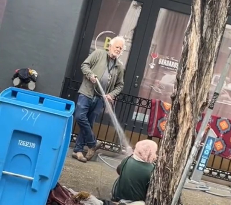 US man spraying water on homeless woman