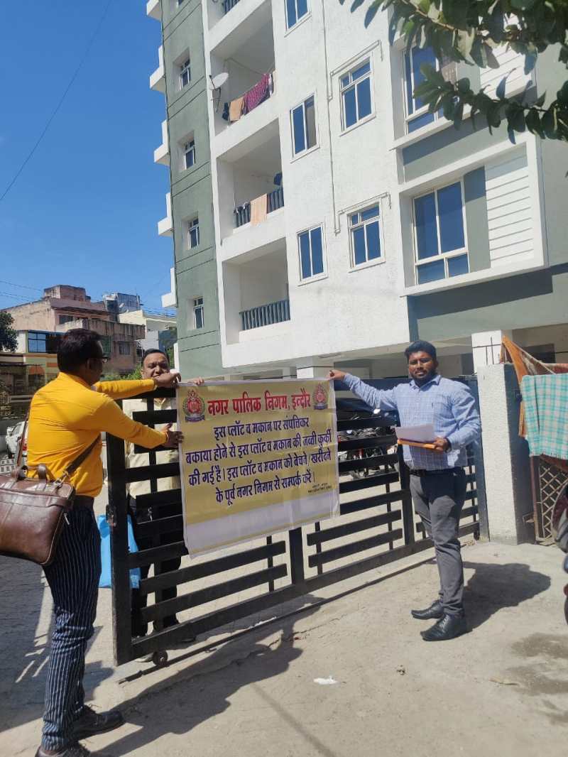 बिल्डिंग और फ्लैट्स की जब्ती का पोस्टर लगाते निगम कर्मचारी