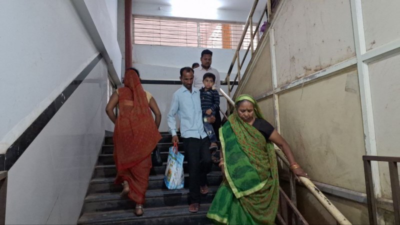 बच्चे को गोद व हाथ में सामान लेकर सीढियां उतरता मरीज का परिजन