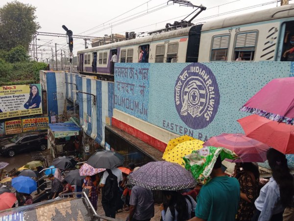 कोलकाता के दमदम स्टेशन के पास बारिश से बचने के लिए छाते का सहारा लिए लोग। 