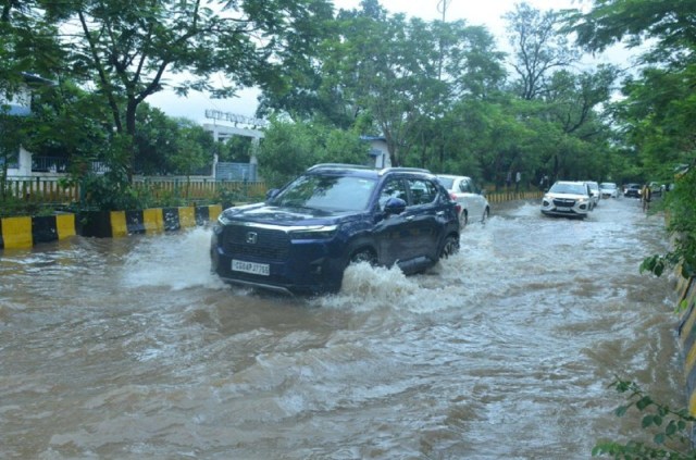 तेज बारिश के बाद जलमग्न सड़क से गुजरते वाहन।