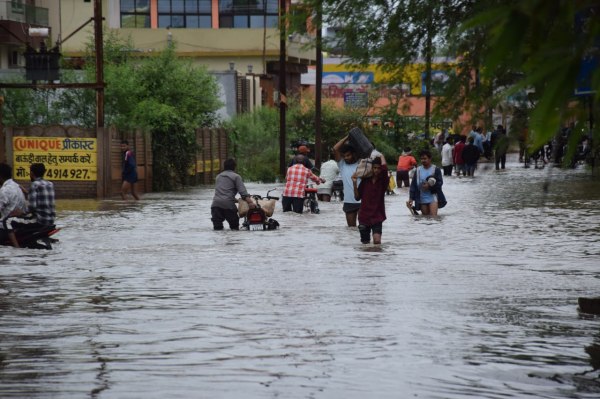 तेज बारिश के बाद जलमग्न सड़क से गुजरते लोग।