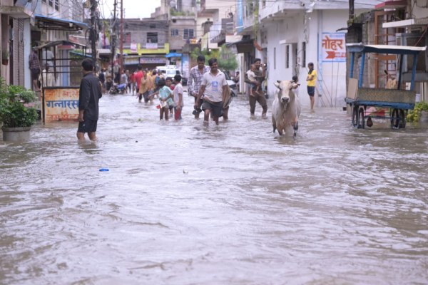 तेज बारिश के बाद जलमग्न सड़क से गुजरते लोग।