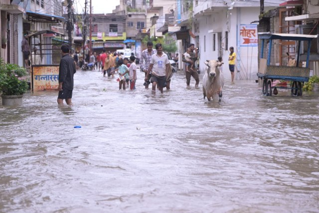 तेज बारिश के बाद जलमग्न सड़क से गुजरते लोग।