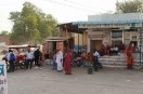 दुकान के आगे टिनशेड नीचे बैठकर बस का इंतजार करते यात्री