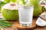 A fresh tender coconut with a straw placed on a rustic wooden table with green leaves in the background