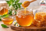 Glass jar of raw honey with wooden honey dipper on a wooden table, representing natural energy and health benefits.