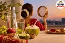 करवा चौथ के लिए सजी महिला के सामने पानी की बोतल, गिलास, नारियल पानी, अंगूर, सेब और खीरे रखे हैं।